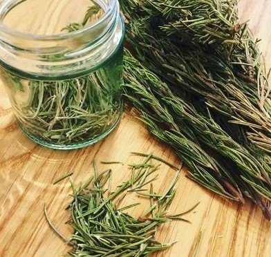 Dried Rosemary in a clear glass jar, on a wooden surface