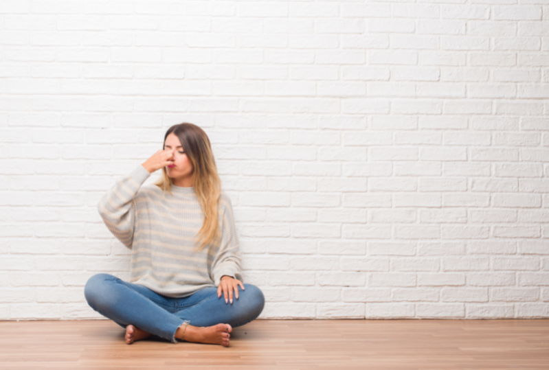 Eco-friendly paint - free image from Canva of a woman sitting in front of a brick wall painted white and holding her nose closed because of the smell 