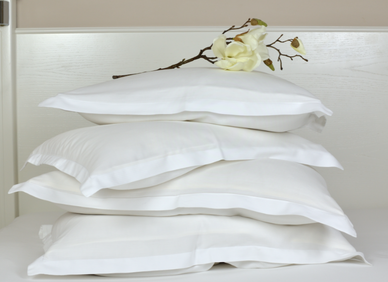 Eco Swaps - Canva image of a stack of white bed pillows with a magnolia flower on top of the pile