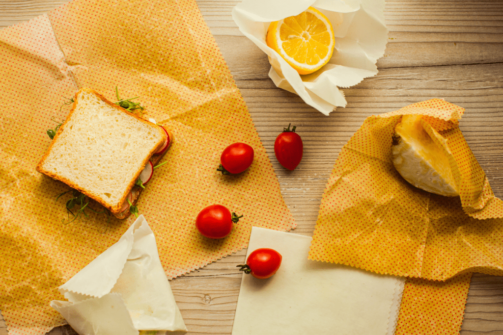 Eco Swaps - Free Canva Image of Yellow Beeswax Wraps with a sandwich, cherry tomatoes and a lemon on a wooden cutting board