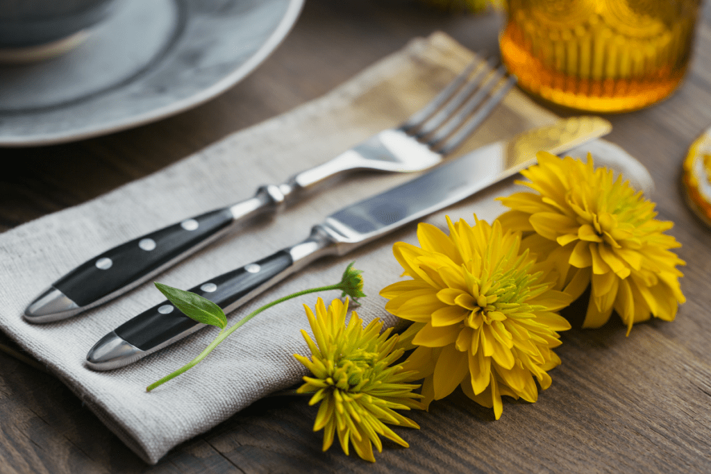 Eco Swaps - Free Image from Canva of Linen Napkins folded next to a place setting with metal cutlery and a yellow flowers