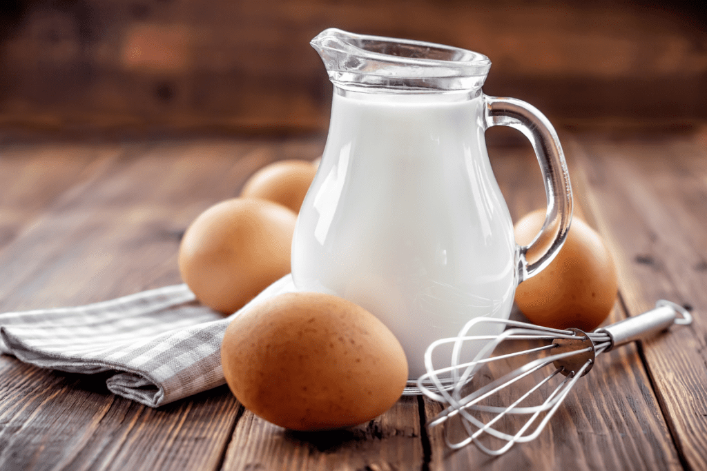 Self-sufficient homes: image of eggs and a glass just of milk on a wooden table, with a metal whisk lying next to it