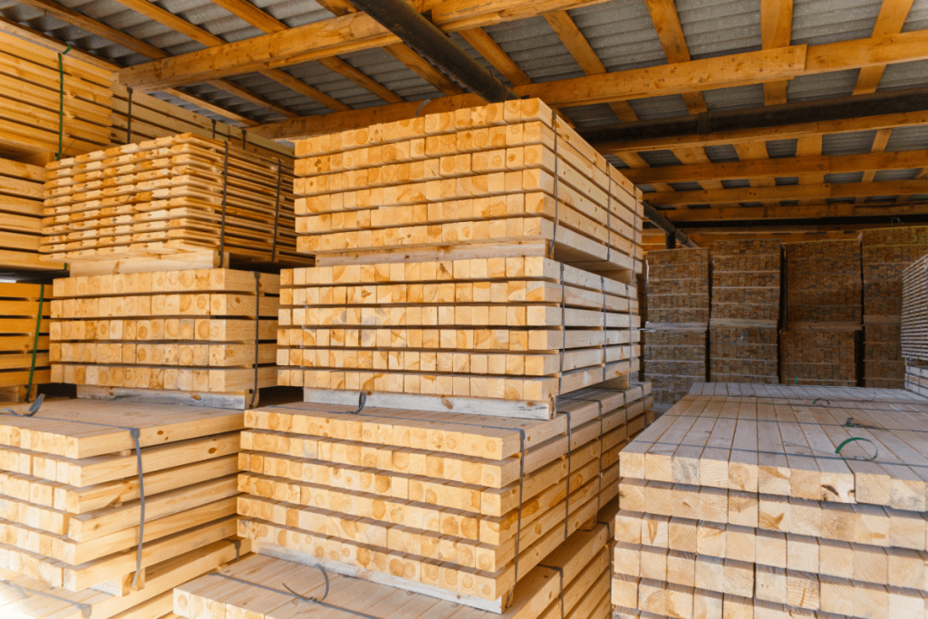 Storing Building Materials - Stacks of neatly piled wooden planks indoors. The pieces are laid out so there is breathing room between each layer and the planks are supported so they don't sag or bend
