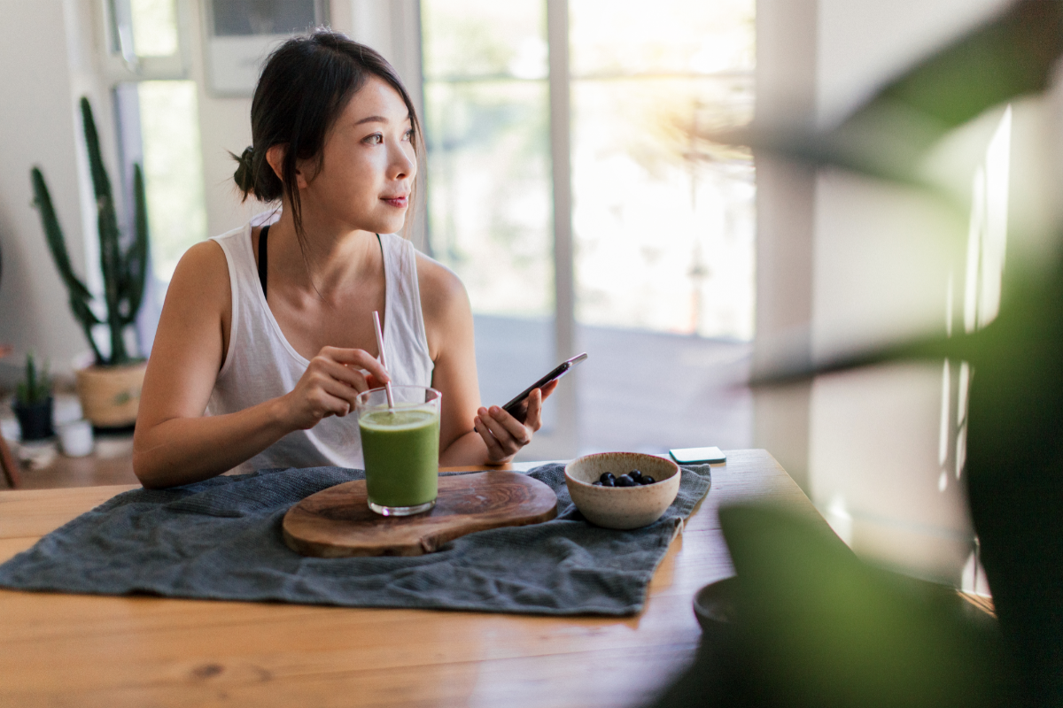 Sustainable Living - stock image from Canva of a woman sitting at a table, drinking a green juice with a paper straw