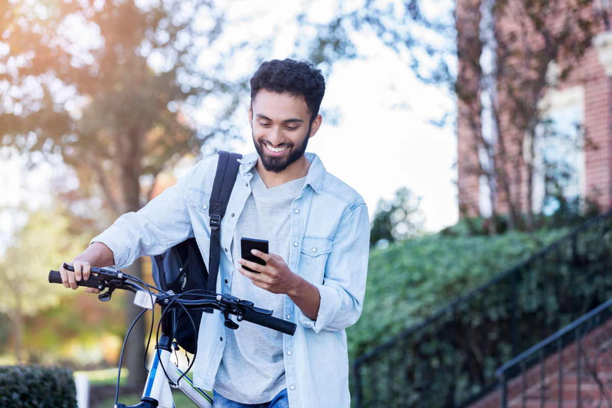 Green Living Tips for College Students- Stock Image from Canva of a Male Students with a bicycle and backpack