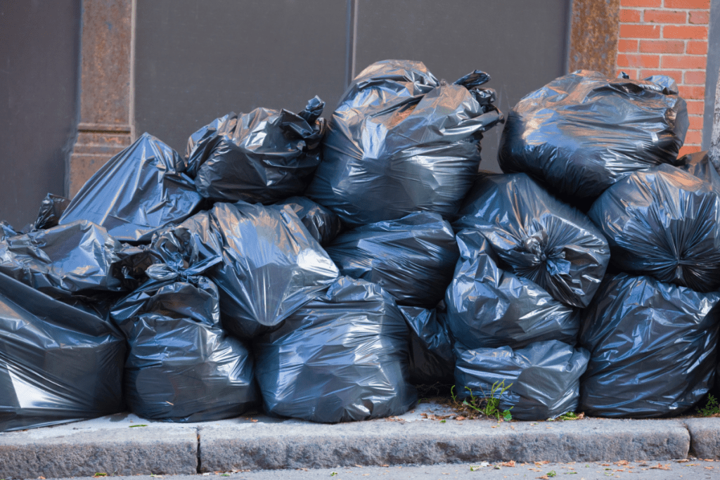 What is a landfill? Image of a large pile of black trash bags on the curb, waiting to be collected to go to landfill