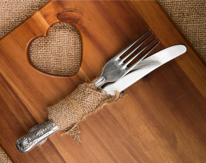 Acacia wood chopping board with a silver knife and fork, wrapped in natural fabric