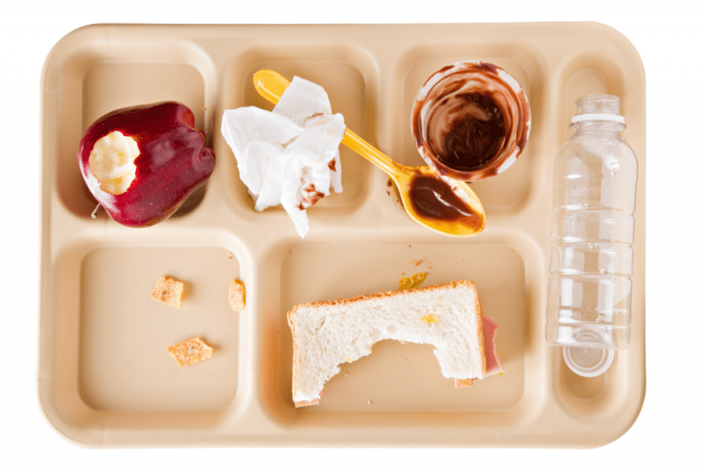 School lunch tray with leftover food, empty plastic water bottle, empty plastic condiment containers and plastic utensils 