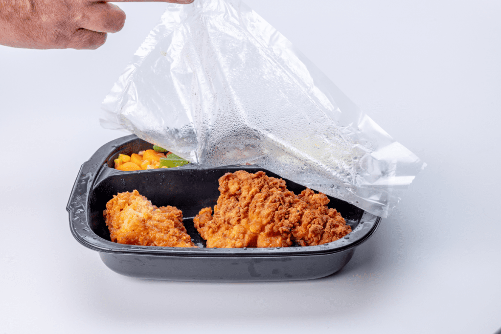 Green Canteens vs Plastic wrapped TV dinners: Image of a microwave meal in plastic with a hand removing the cellophane sheet off the top