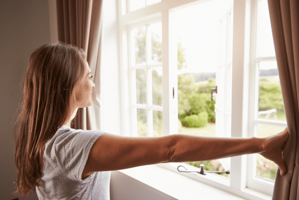 Indoor Air Quality - Stock image of a woman Opening Windows in the morning