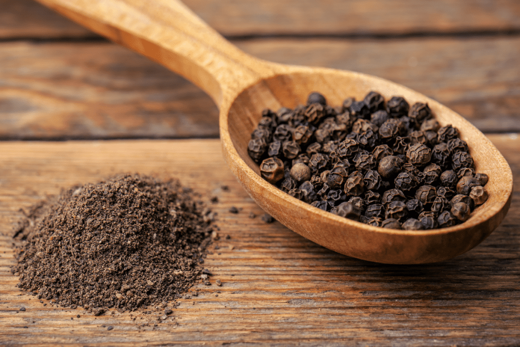 Herbs for Weight Loss - Ground Black Pepper next to a wooden spoon of whole black pepper corns