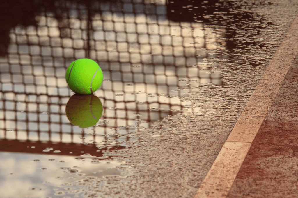 Weather Forecasting - Image of a wet tennis court and a lone, wet tennis ball on the ground