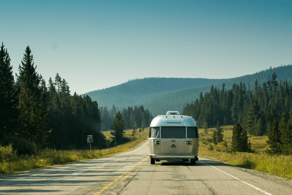 Eco-friendly trailer conversion - stock image from Canva of an Airstream viewed from behind driving down a country road in the wilderness