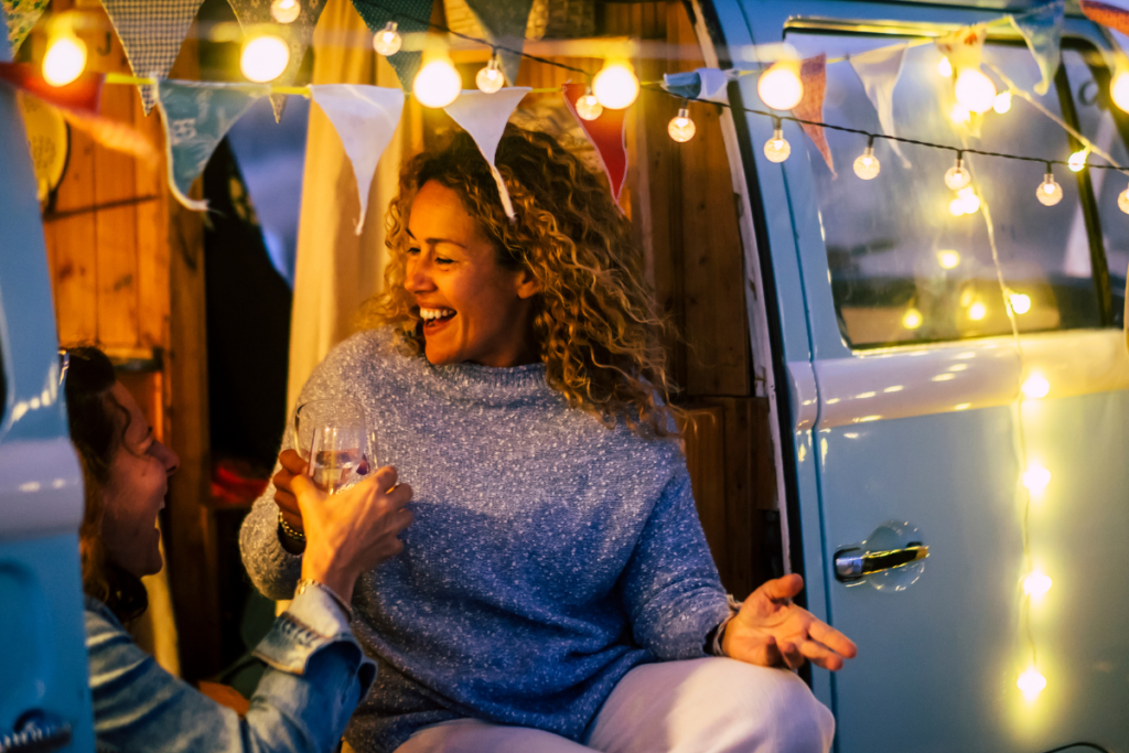 Eco-friendly trailer conversion - stock image from Canva of a trailer with fairy lights and bunting and a happy couple laughing