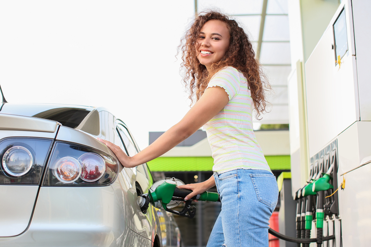 How to Improve Your Fuel Economy - Stock Image from Canva of a young woman smiling while putting filling her gas tank