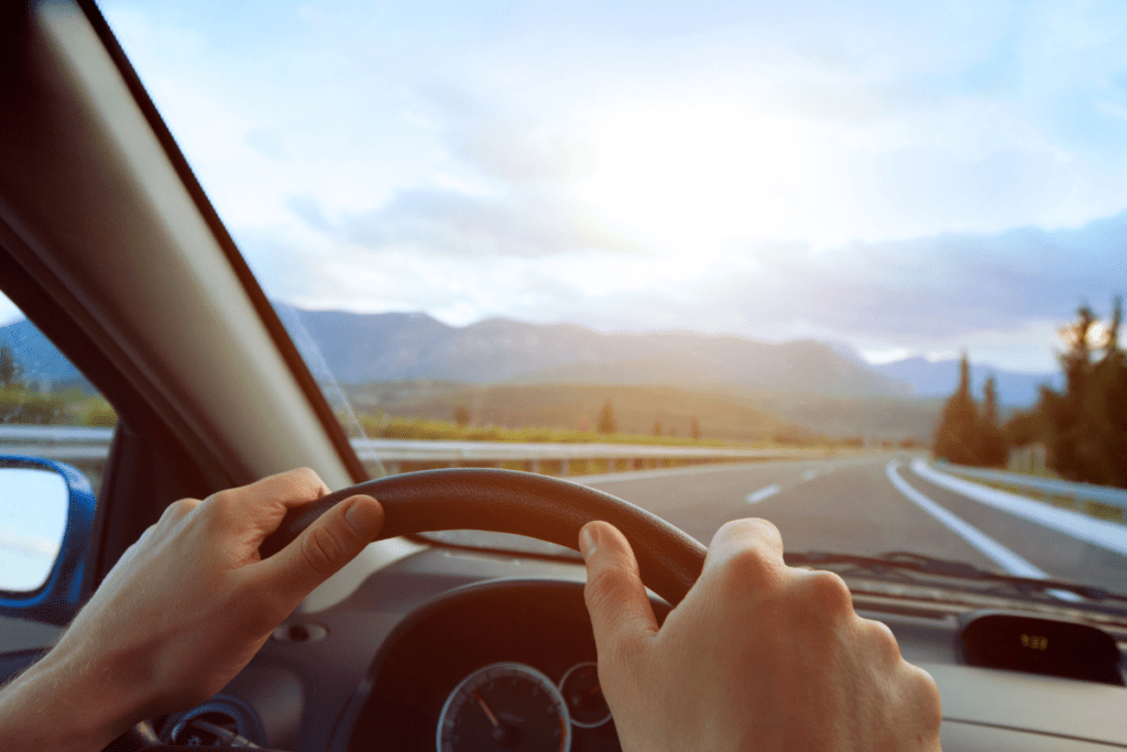 How to Improve Your Fuel Economy - Stock Image from Canva of a drivers hands on the wheel, with a country landscape visible through the windscreen