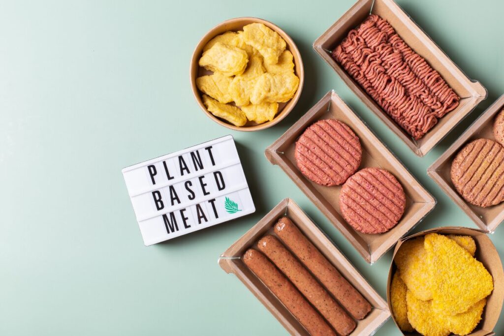 Selection of plant-based meat products, including burger patties, sausages, and mince on platters