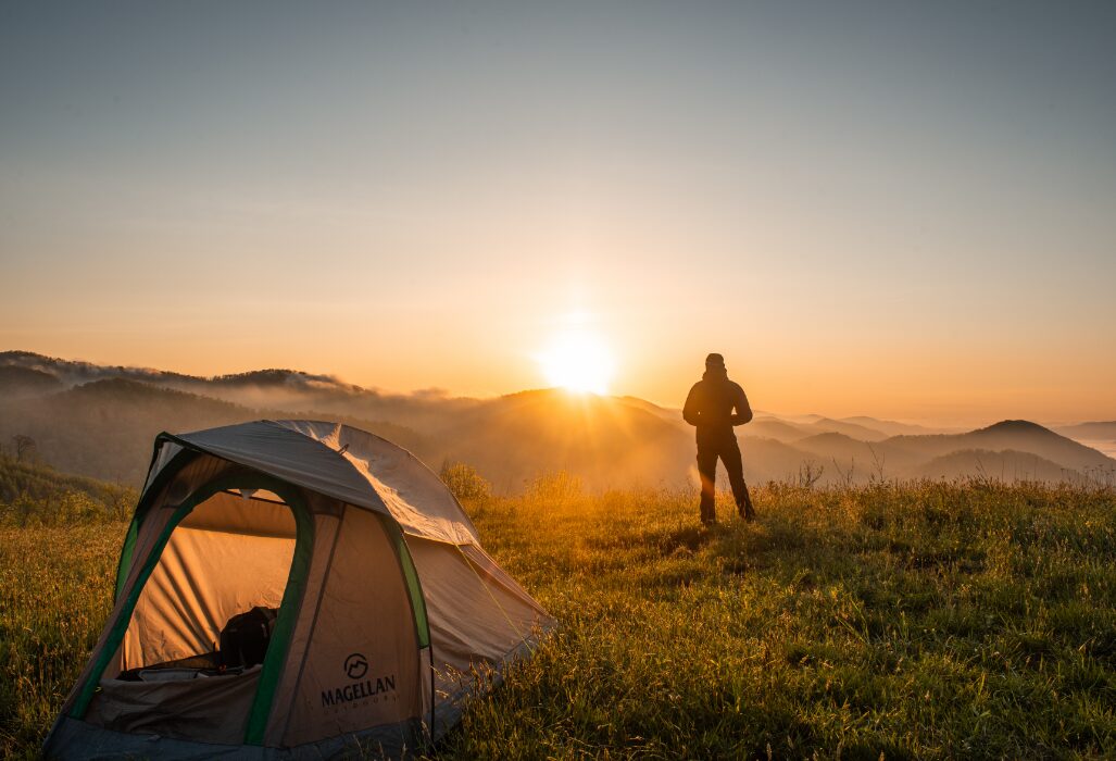 eco-camping - man stands on a clear green heath, looking out at the sunrise