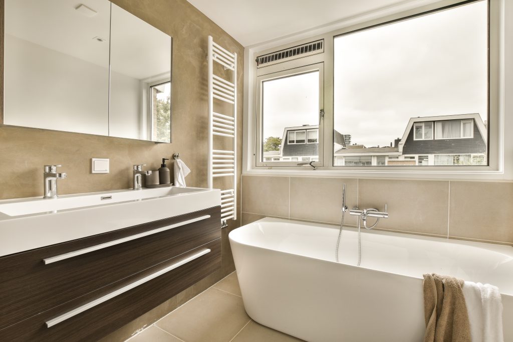 a bathroom with a bathtub, sink and mirror in the corner next to it is a window that looks out onto the street