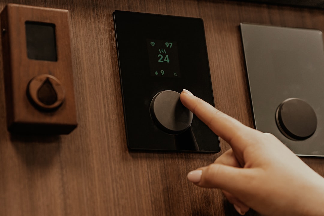 a hand adjusting a black digital thermostat